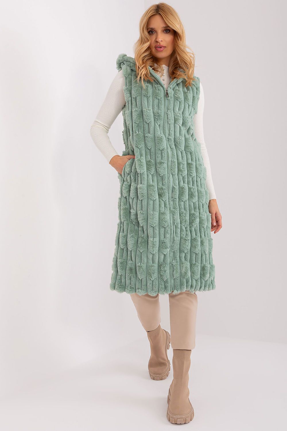 Woman wearing a green textured vest over a white long-sleeve shirt on a white background