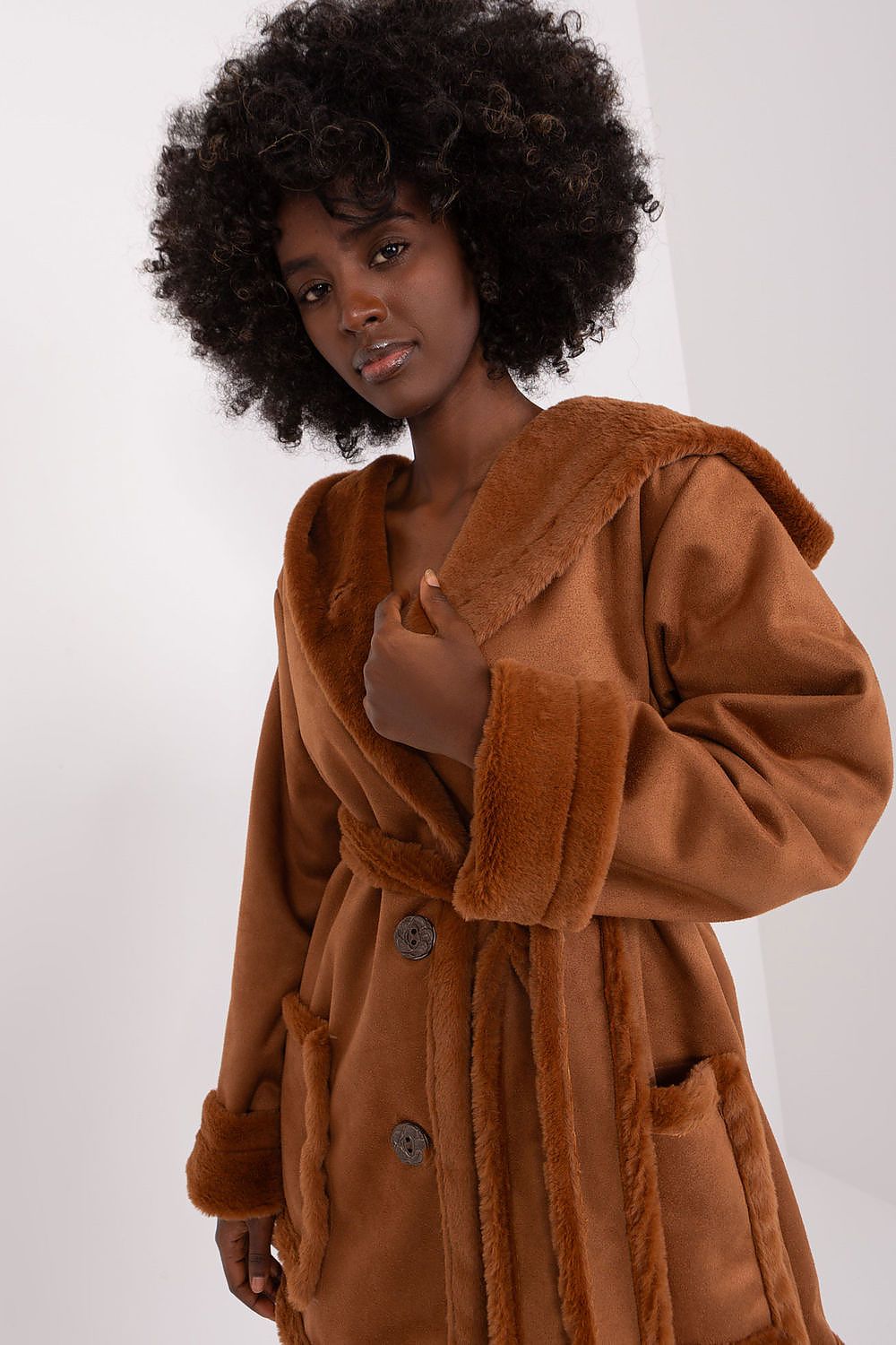 A woman modeling a beige coat with a hood and tie belt, made of cotton, polyester, and spandex materials.