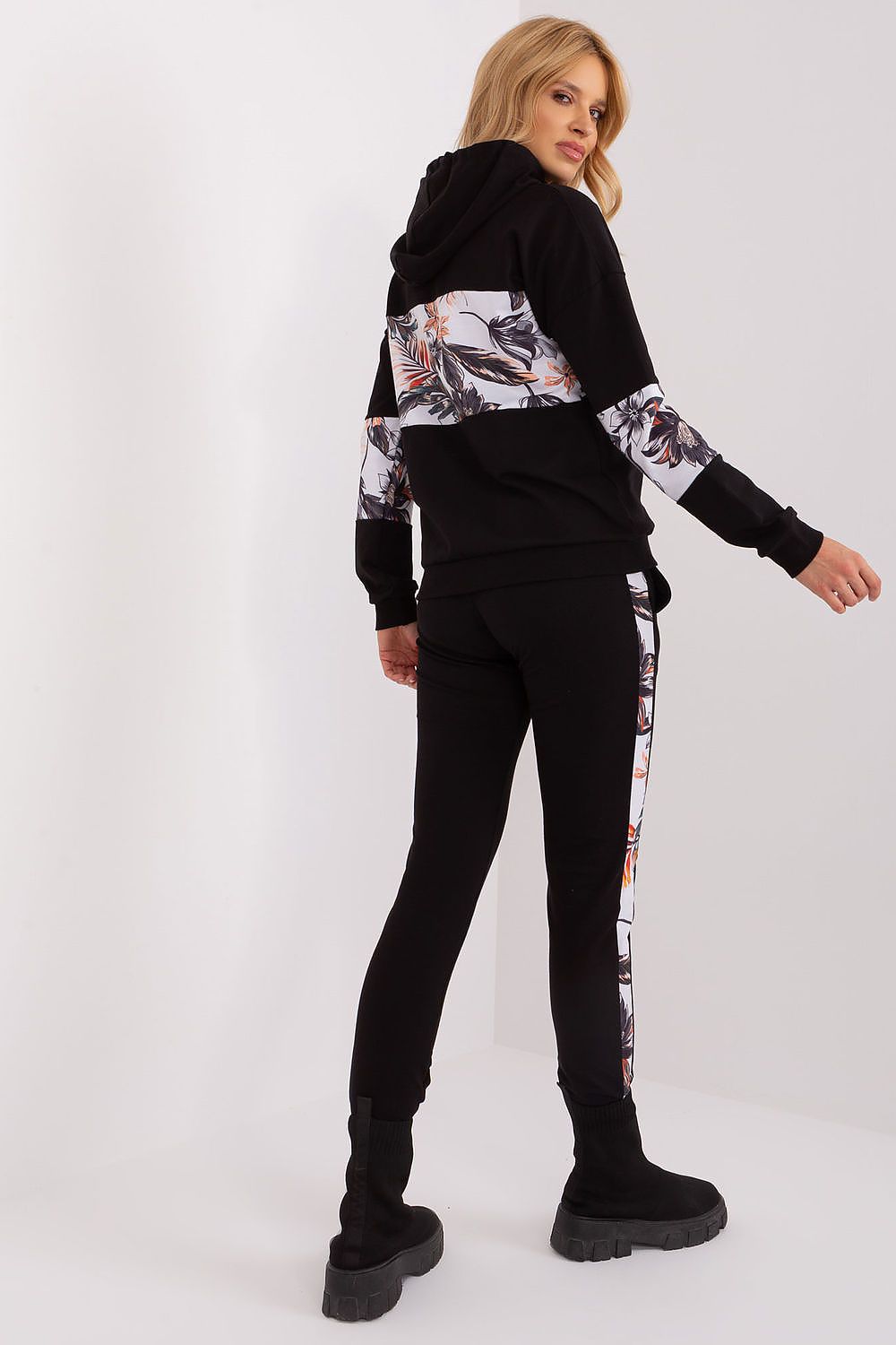 Woman wearing a black hoodie with floral patterns and black pants on a white background