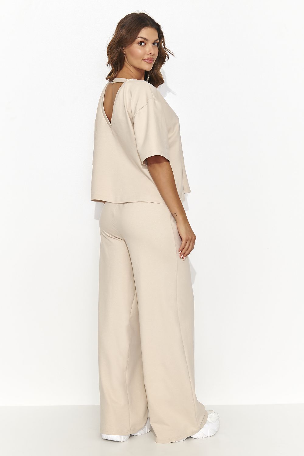 Woman wearing a beige outfit with wide-leg pants on a white background