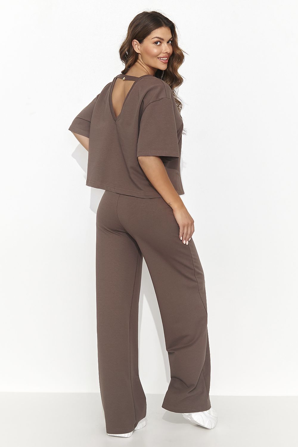 Woman wearing a brown outfit with a backless top and wide-leg pants on a white background