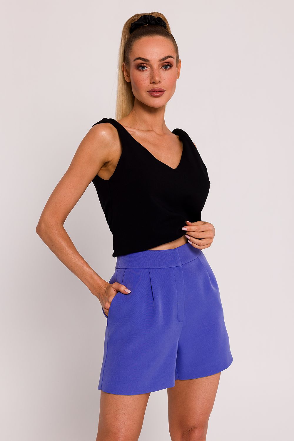 Woman wearing a black sleeveless top and blue shorts against a plain background