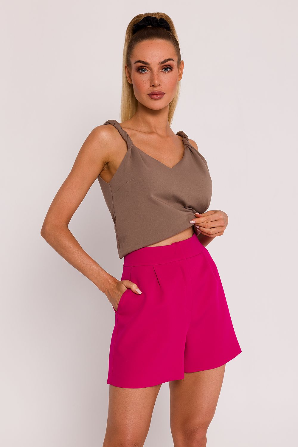 Woman wearing a brown top and pink shorts on a plain background