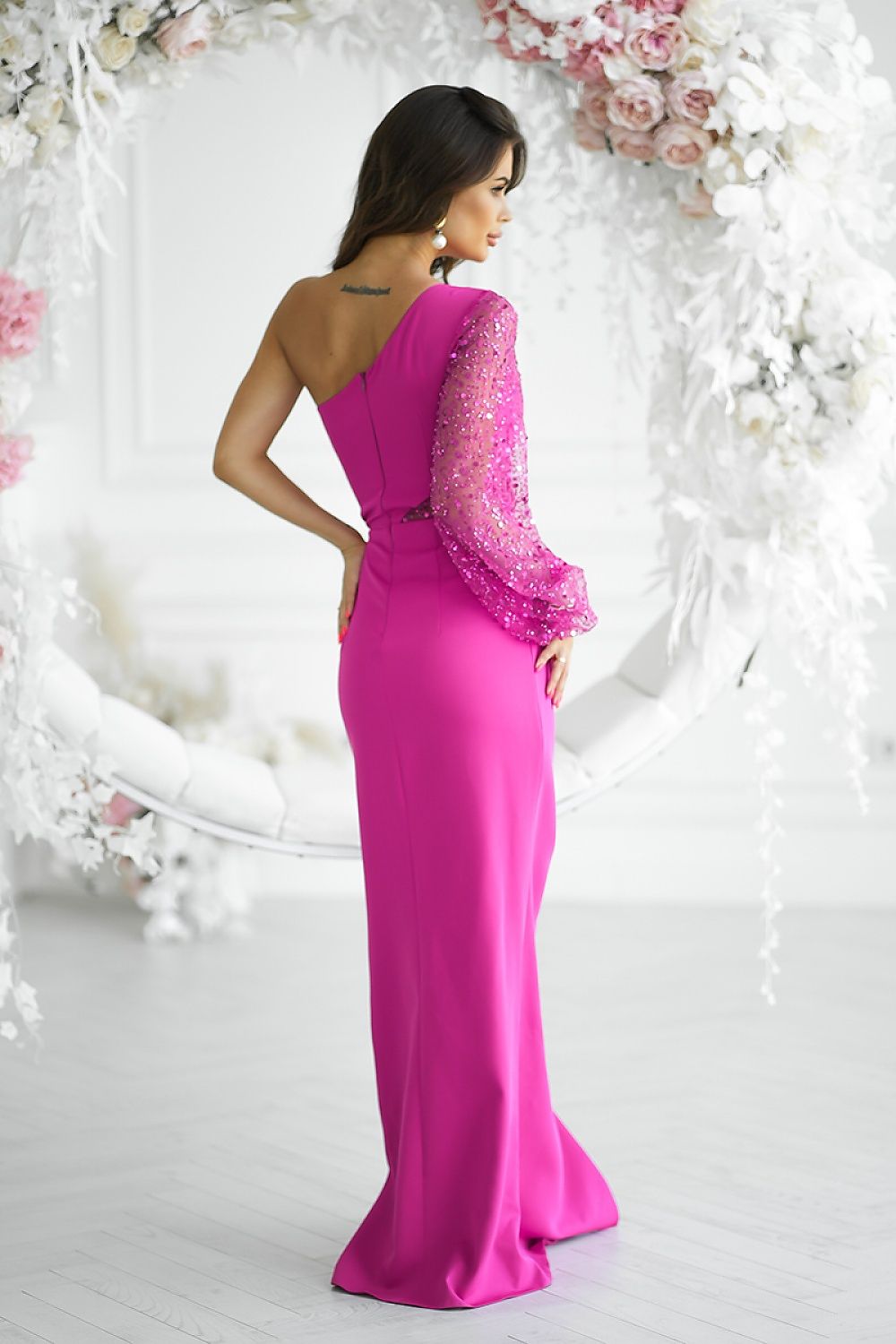 Woman wearing a pink evening gown with floral detailing against a floral backdrop