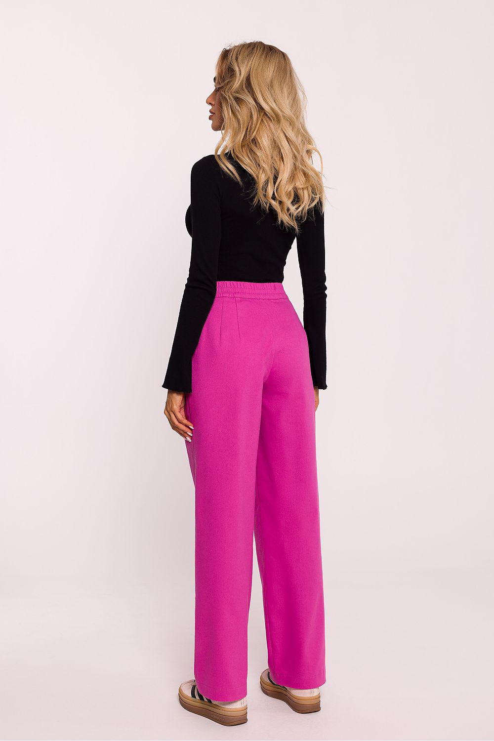 Person wearing a black top and bright pink pants on a light pink background