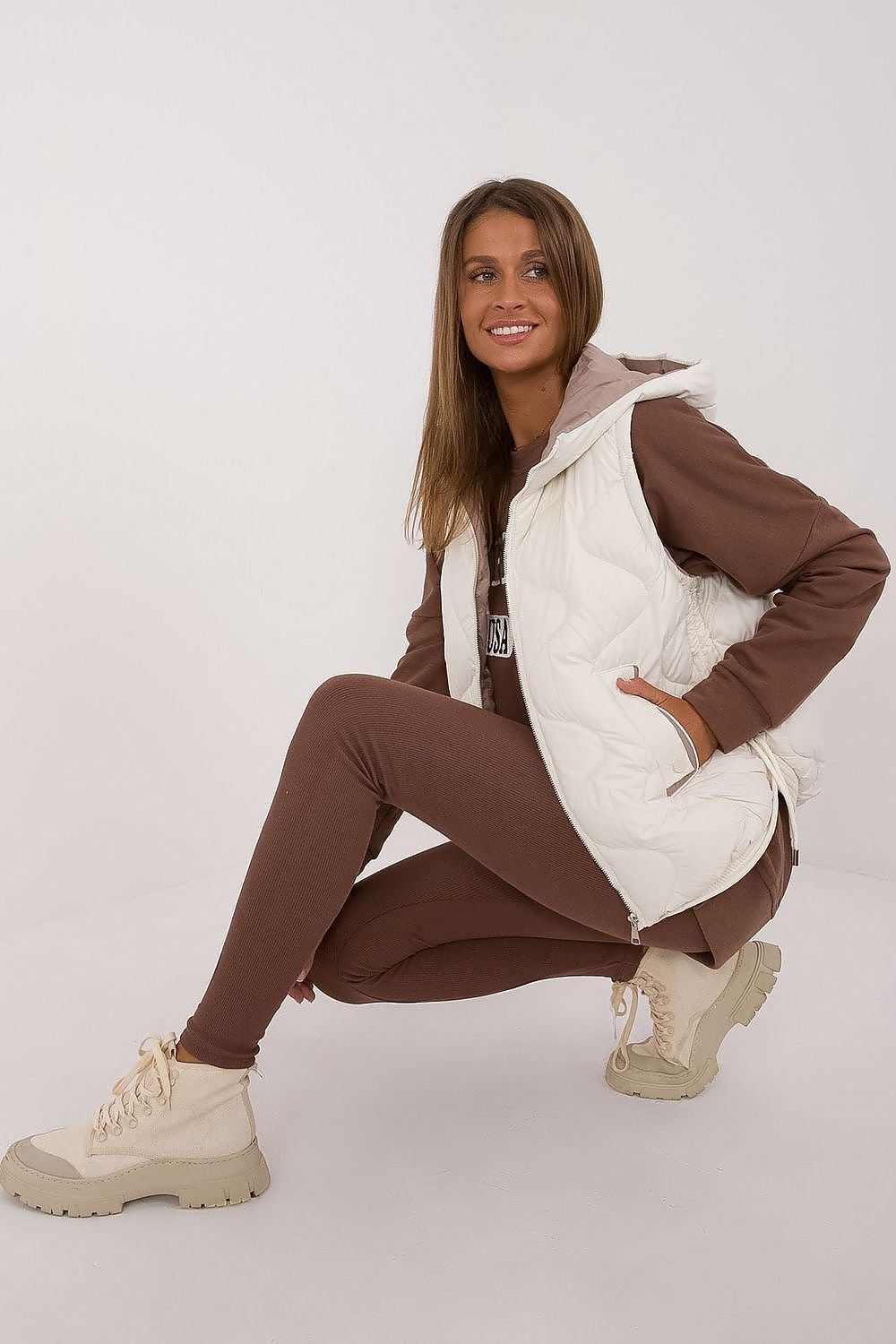 Woman wearing a brown tracksuit with a white puffer vest on a white background