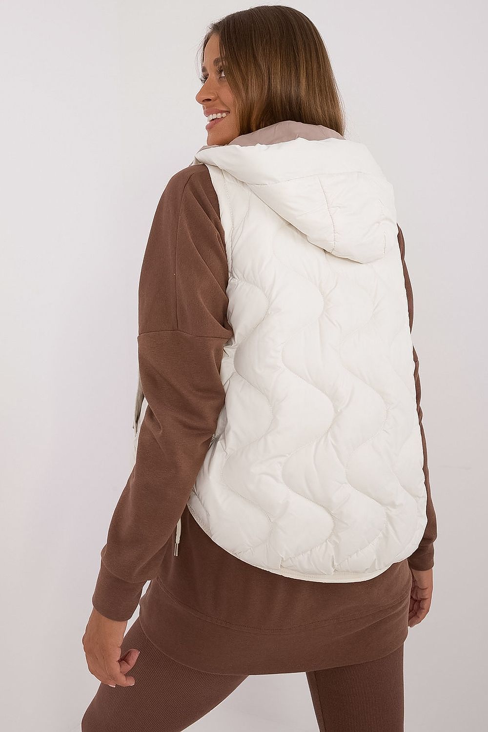Woman wearing a white puffer vest over a brown outfit on a white background