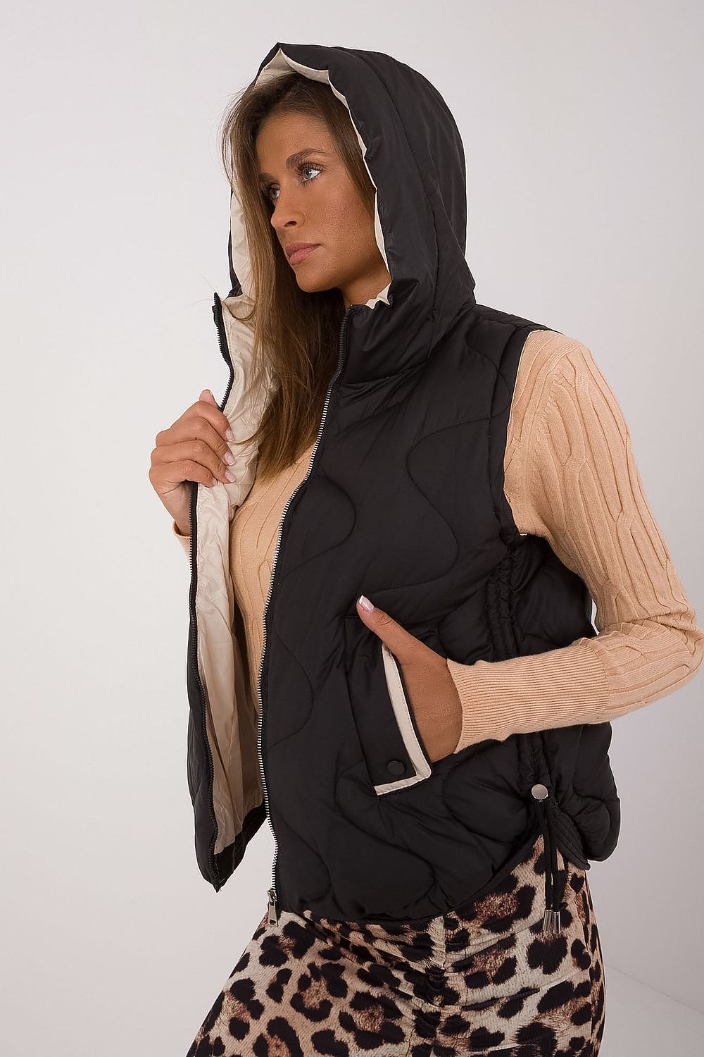 Woman wearing a black hooded vest over a beige sweater with a leopard print skirt on a white background