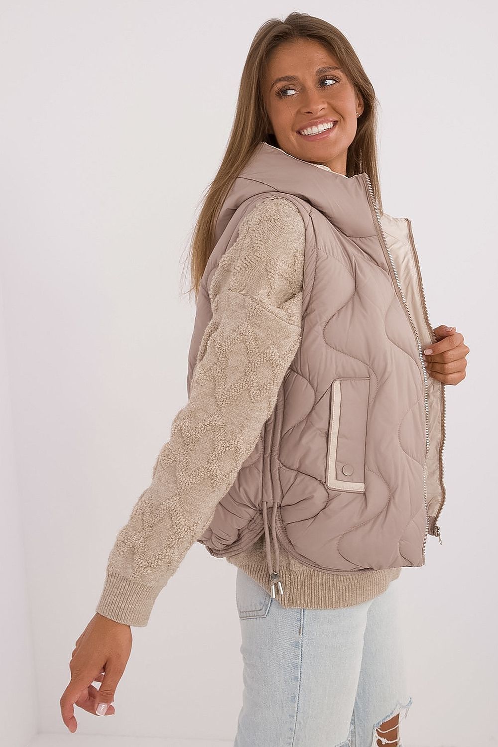 Woman wearing a beige quilted vest over a beige sweater on a white background