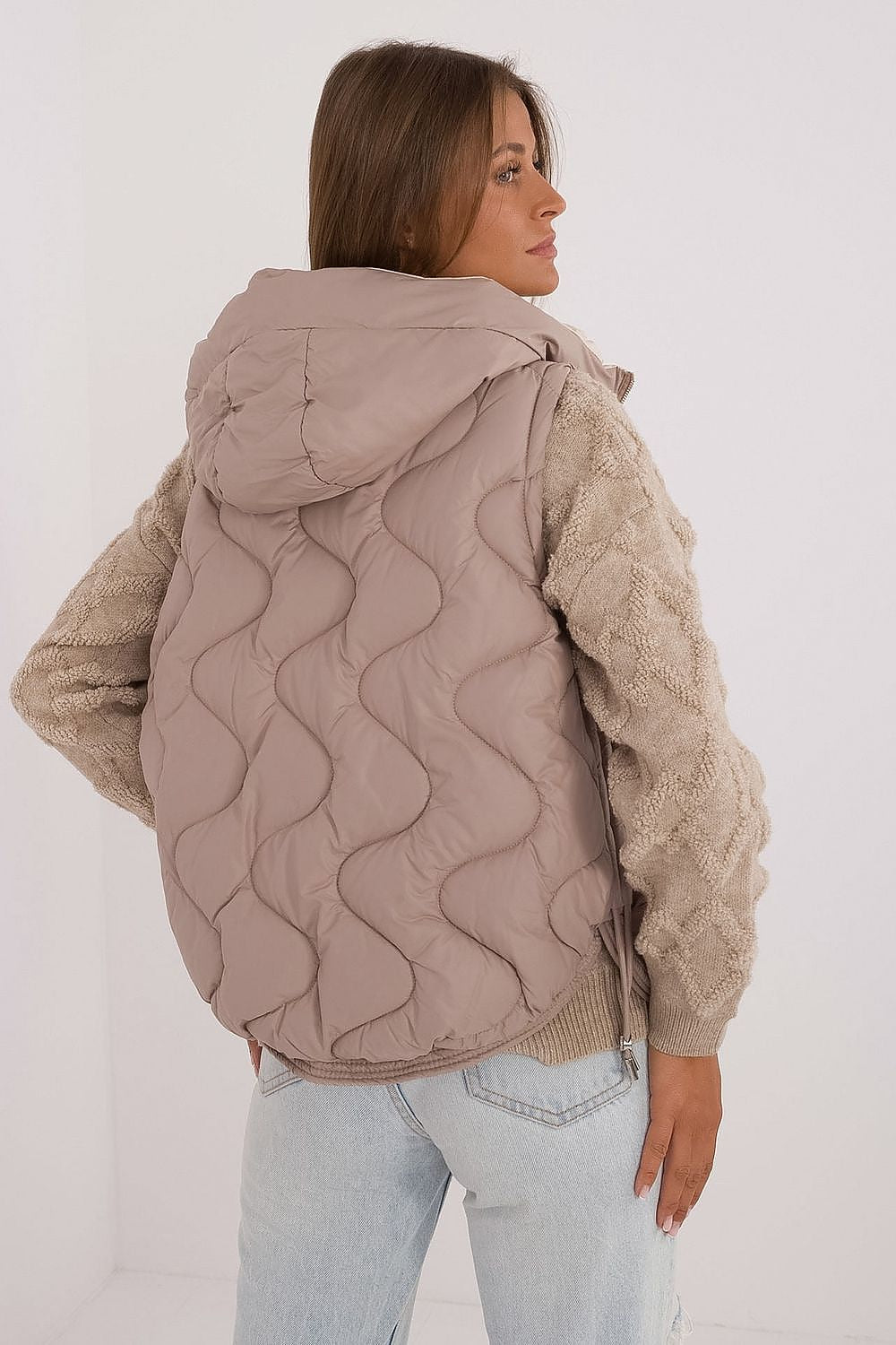 Woman wearing a beige quilted jacket with a plain background