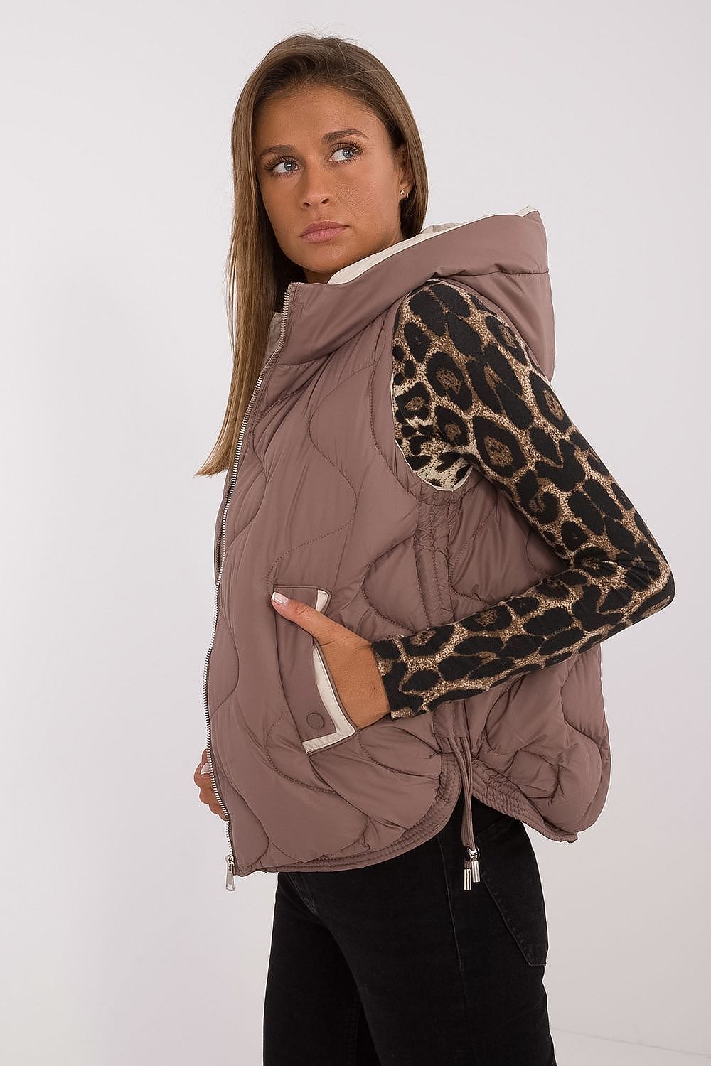 Woman wearing a brown quilted vest with leopard print sleeves on a white background
