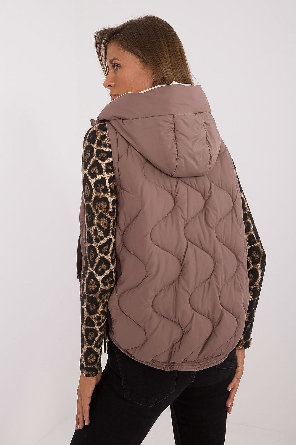 Woman wearing a quilted brown vest over a leopard print long-sleeve shirt on a white background
