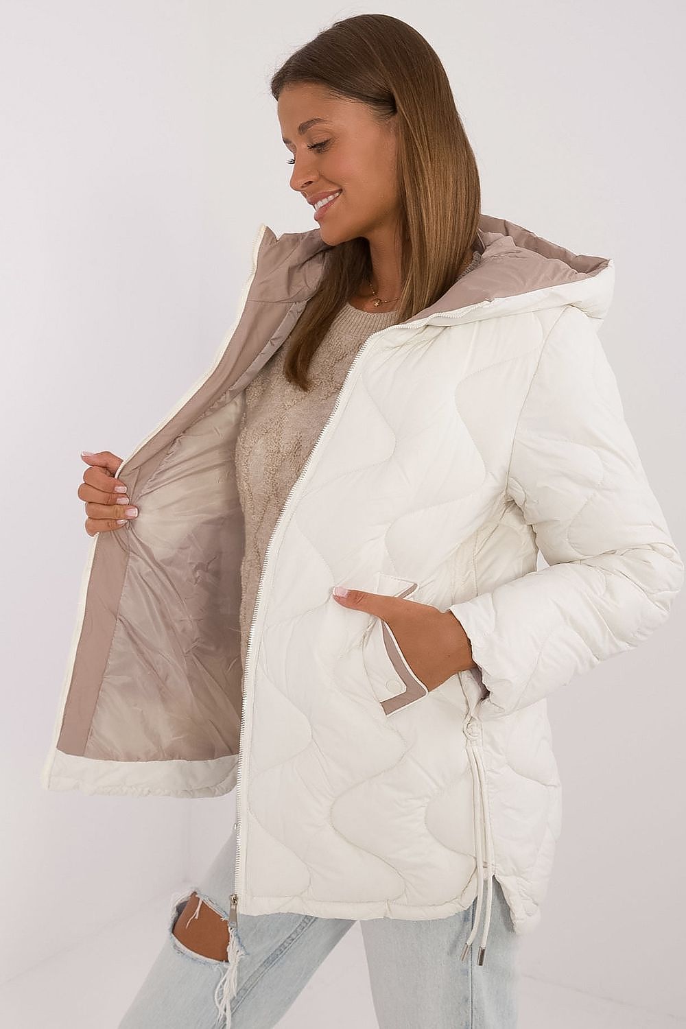 Woman wearing a white puffer jacket with a hood on a plain background