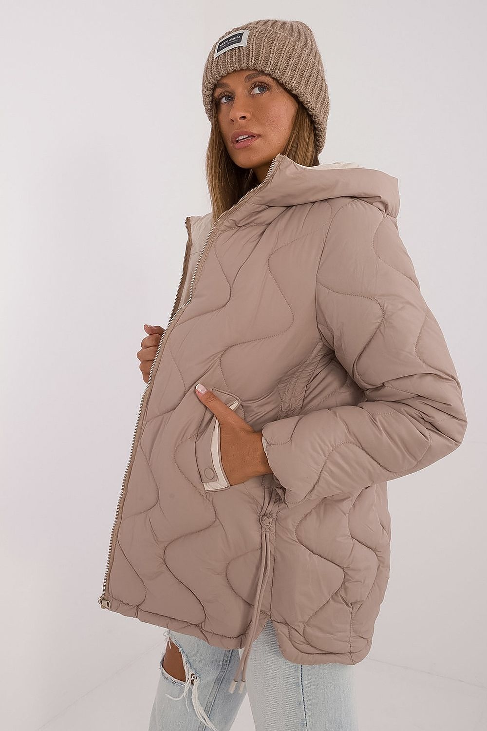 Woman wearing a beige quilted jacket and matching beanie on a white background