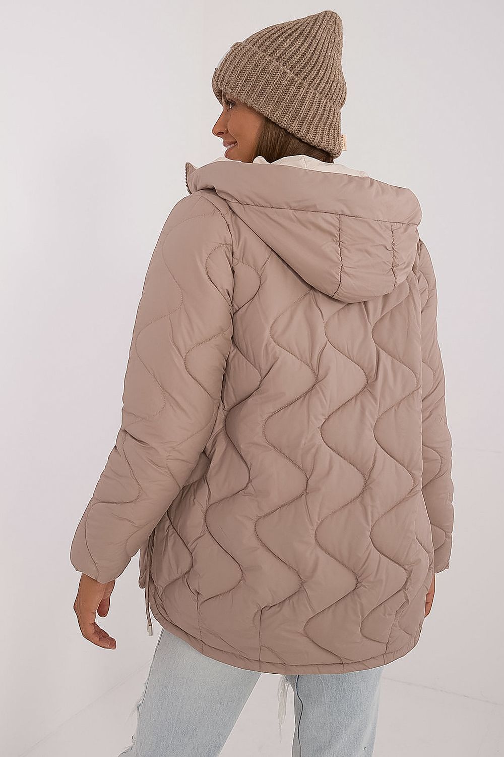 Person wearing a beige quilted jacket and beanie on a white background