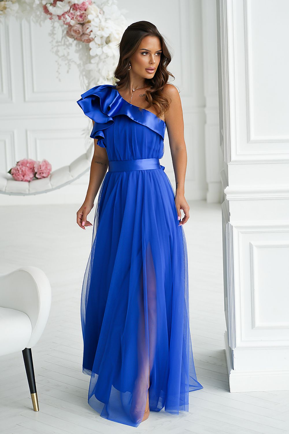 Woman wearing a blue one-shoulder dress in a white room with decorative elements.