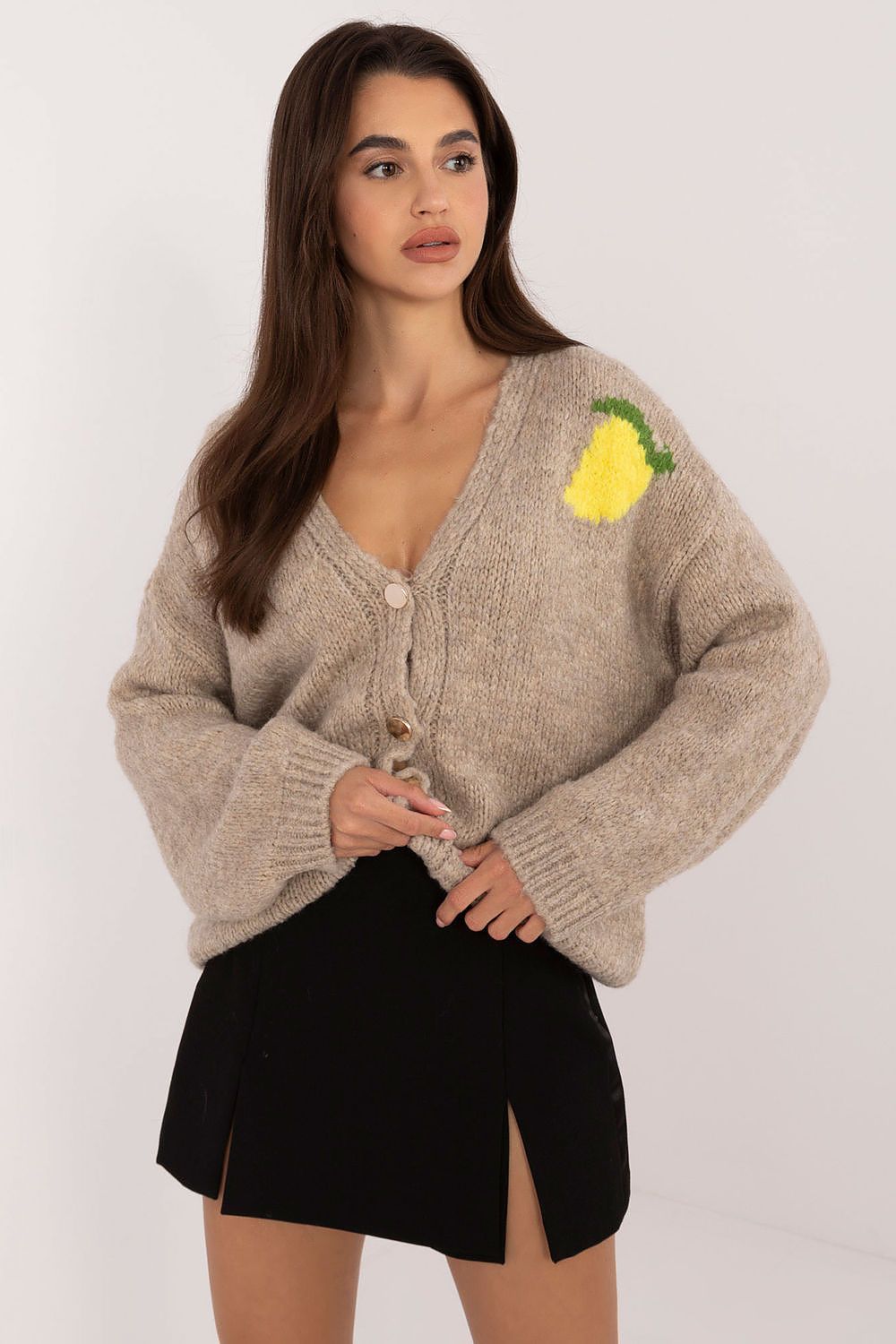 Woman wearing a beige cardigan with a pineapple patch on a white background