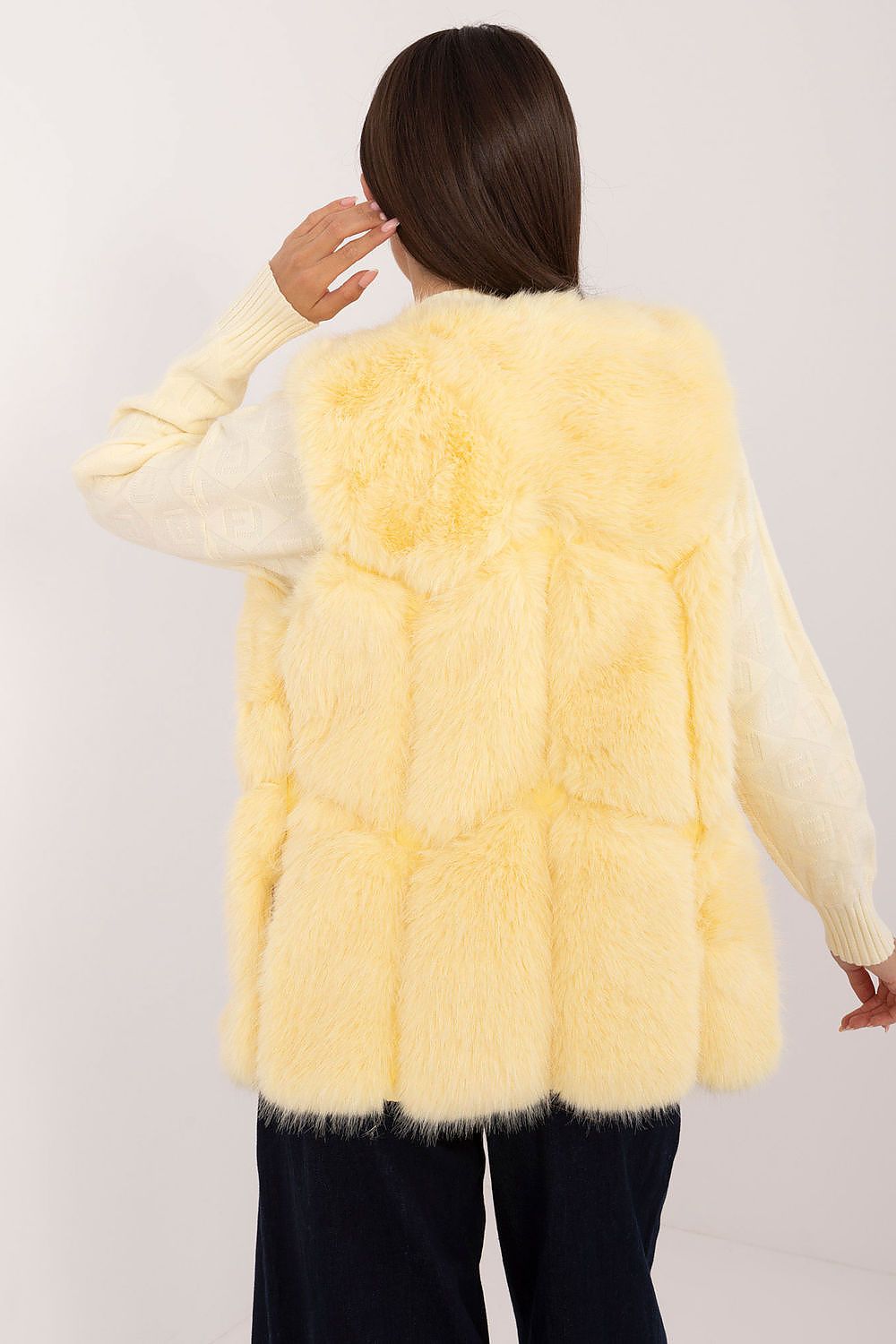 Person wearing a light yellow fur vest over a white sweater on a plain background
