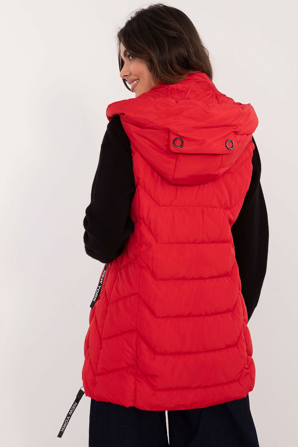 A woman wearing a bright red puffer vest with a hood, shown from the back against a plain light background.