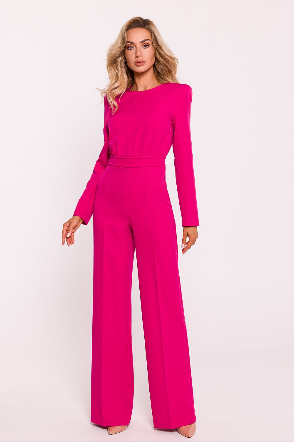 Woman wearing a bright pink jumpsuit on a light pink background
