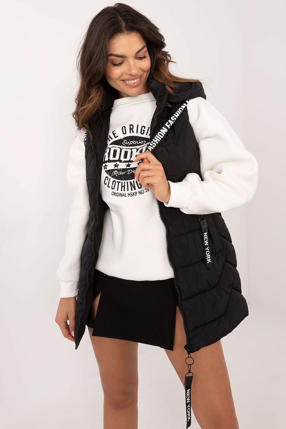 Woman wearing a black and white varsity jacket with a white shirt underneath on a plain background