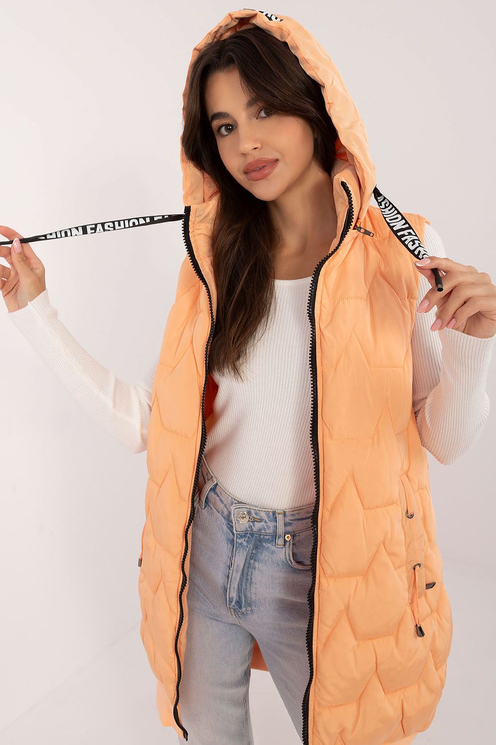 Woman wearing an orange puffer vest with a white background