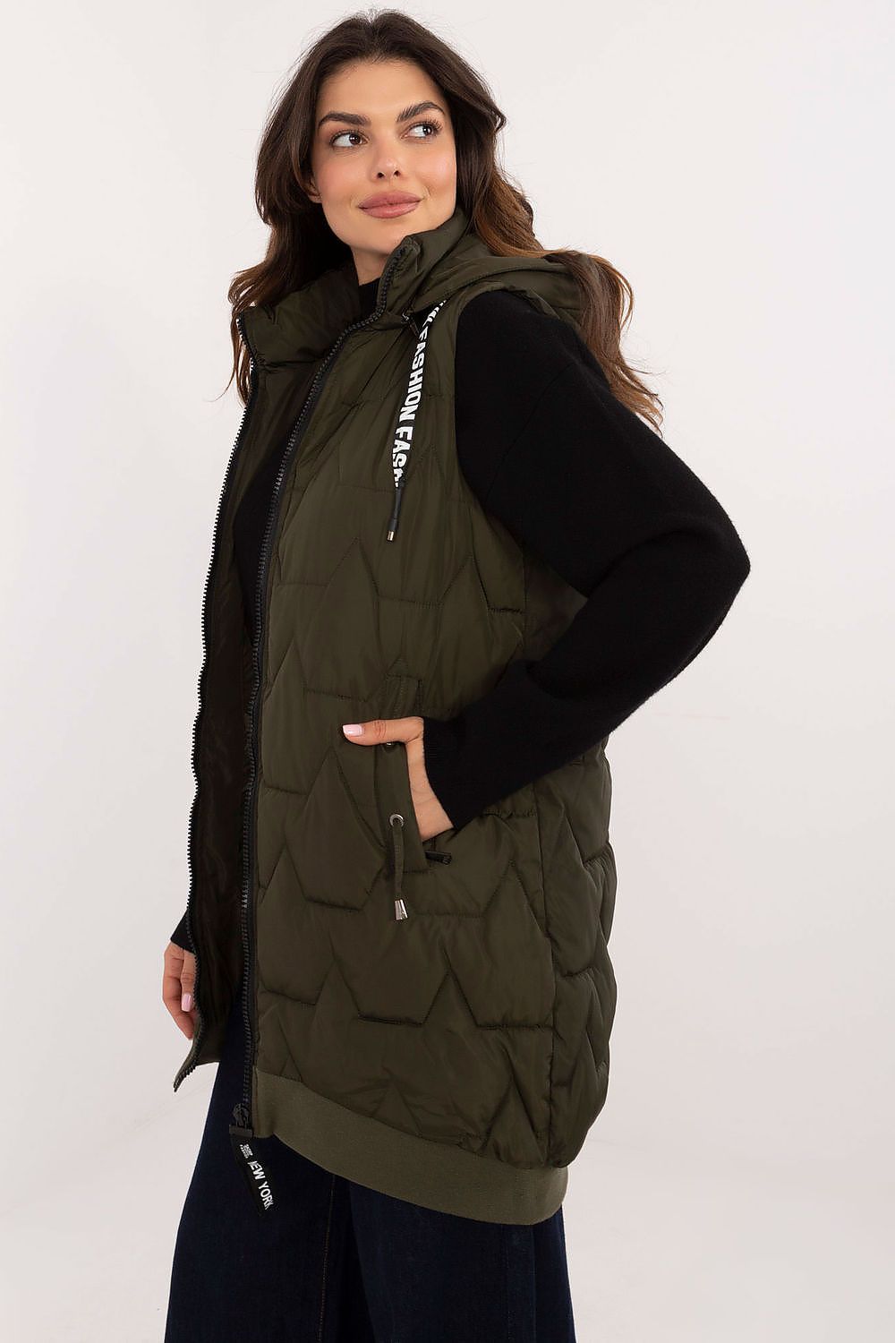 Woman wearing a green quilted vest over a black long-sleeve shirt on a white background