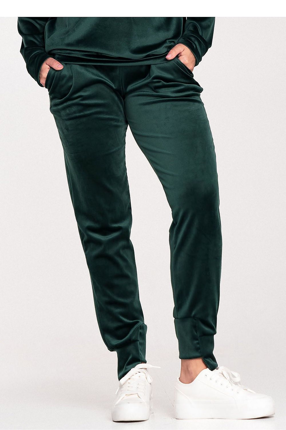 Person wearing dark green jogger pants and white sneakers on a light gray background