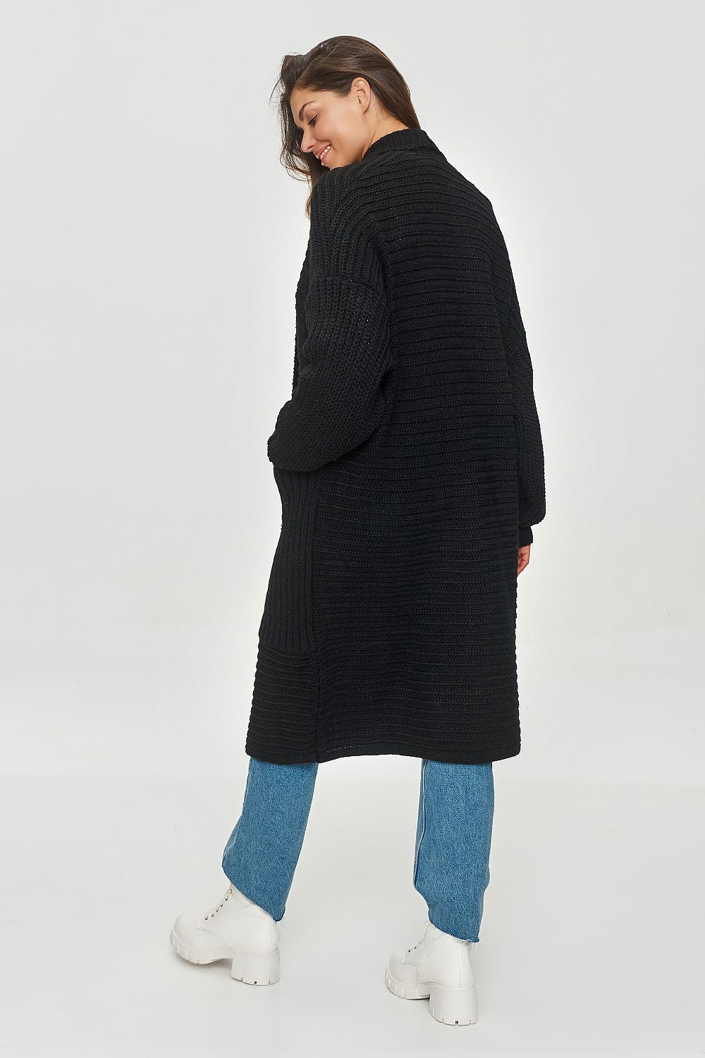 Person wearing a long black ribbed sweater with blue jeans and white shoes on a white background