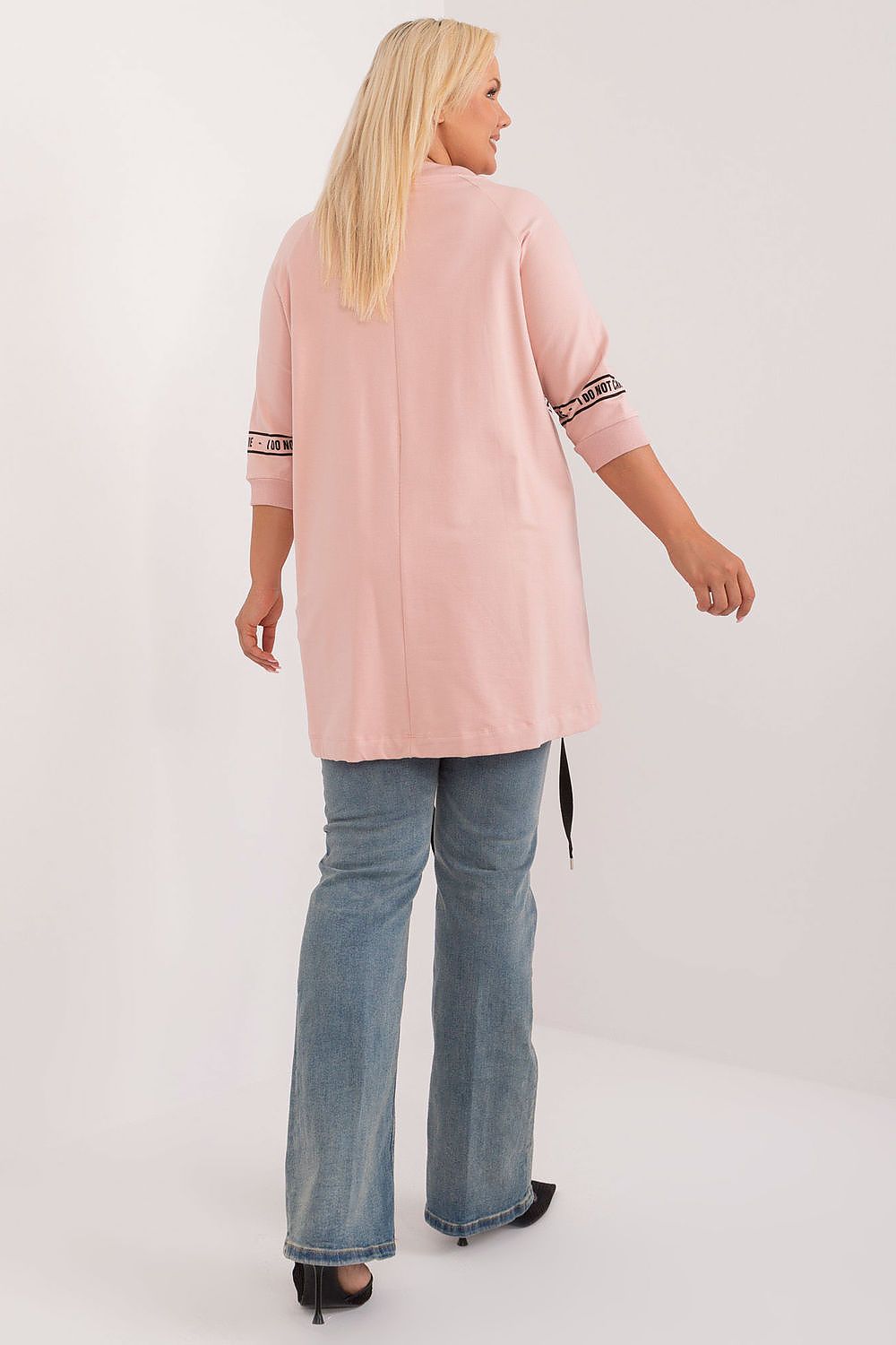 Woman wearing a pink tunic with rolled-up sleeves and blue jeans on a white background