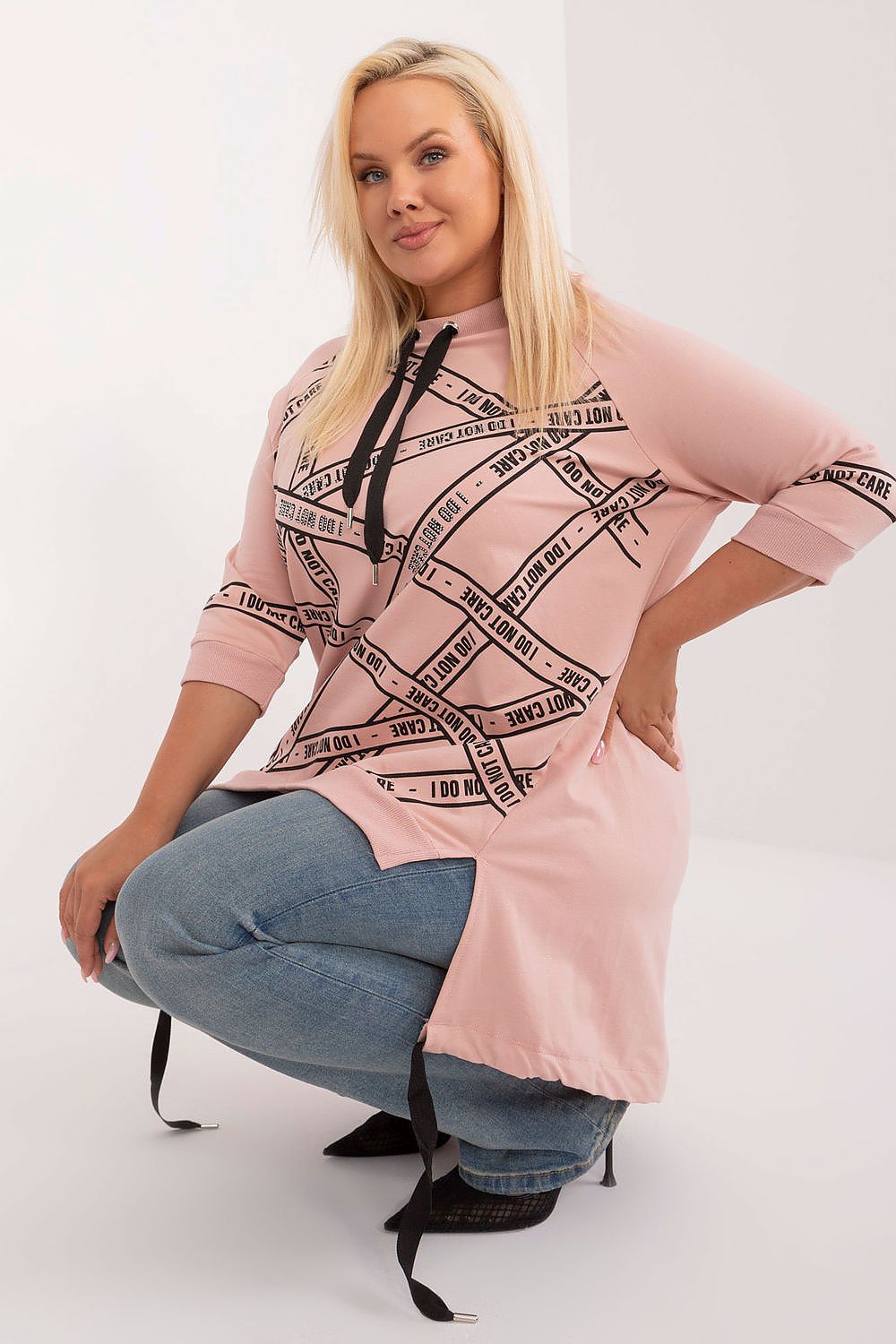 Woman wearing a pink hoodie with black graphic design and blue jeans on a white background