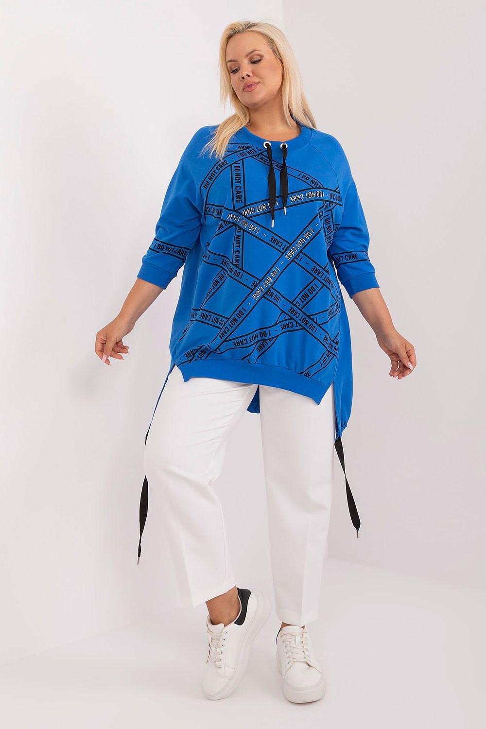 Woman wearing a blue top with black abstract design and white pants on a white background