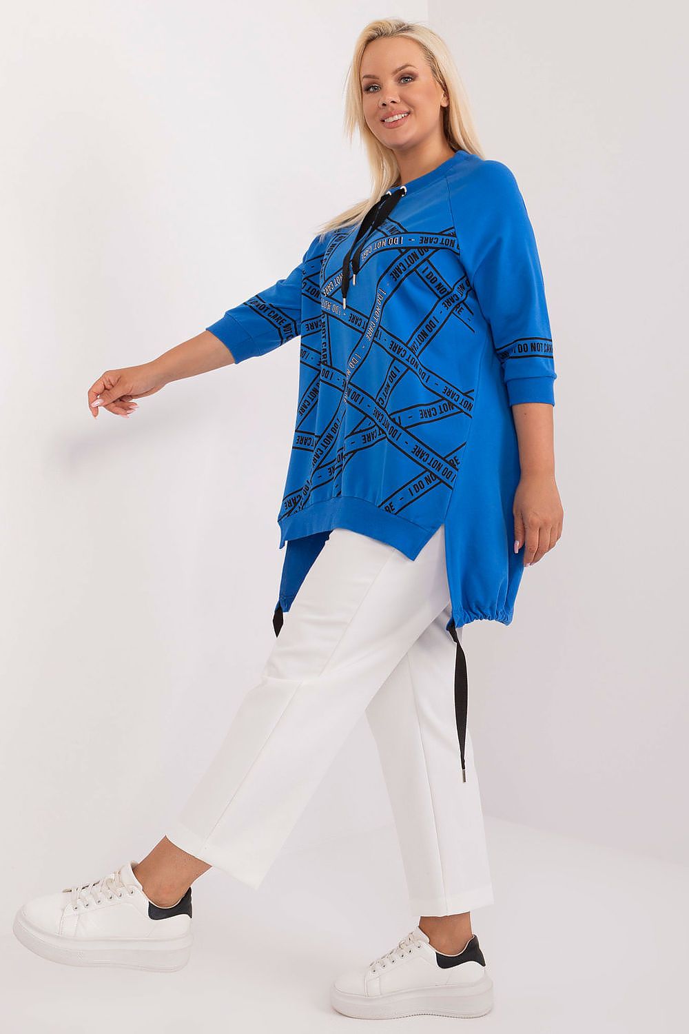 Woman wearing a blue patterned top and white pants on a white background