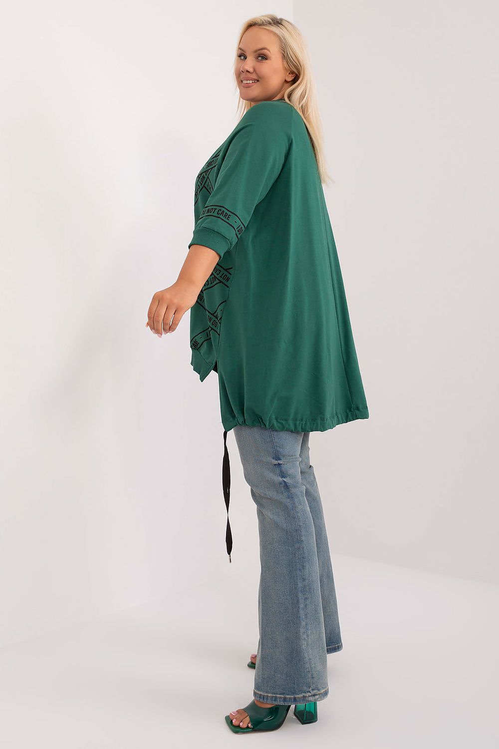 Woman wearing a green kimono-style top and jeans on a white background