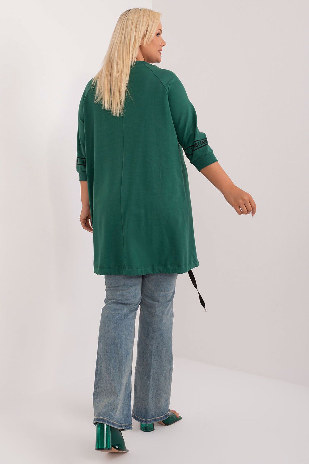 Woman wearing a green long-sleeve top and blue jeans on a white background