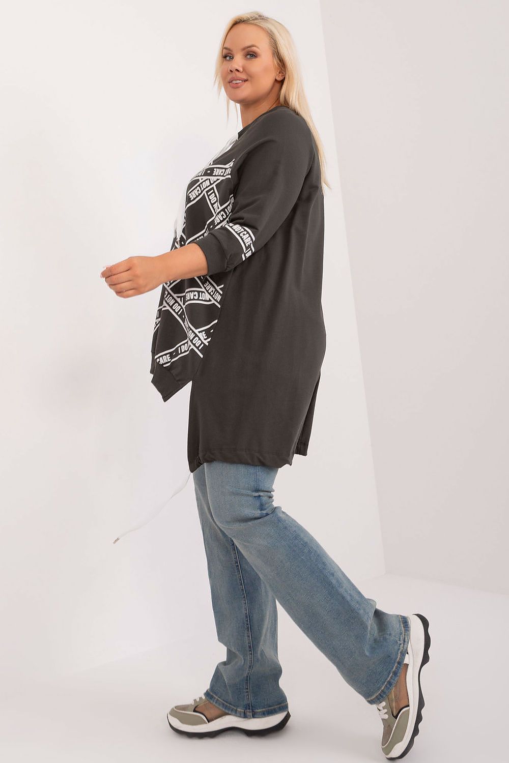 Woman wearing a dark gray cardigan with a patterned design, blue jeans, and sneakers on a white background