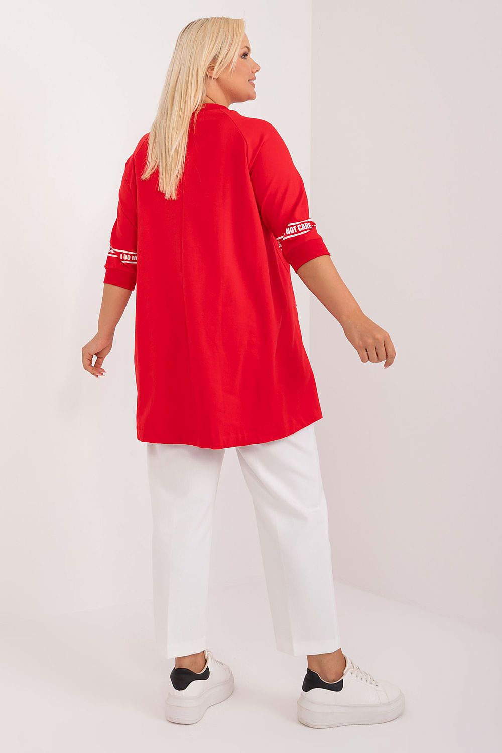 Person wearing a red long-sleeve top with white text and white pants on a white background