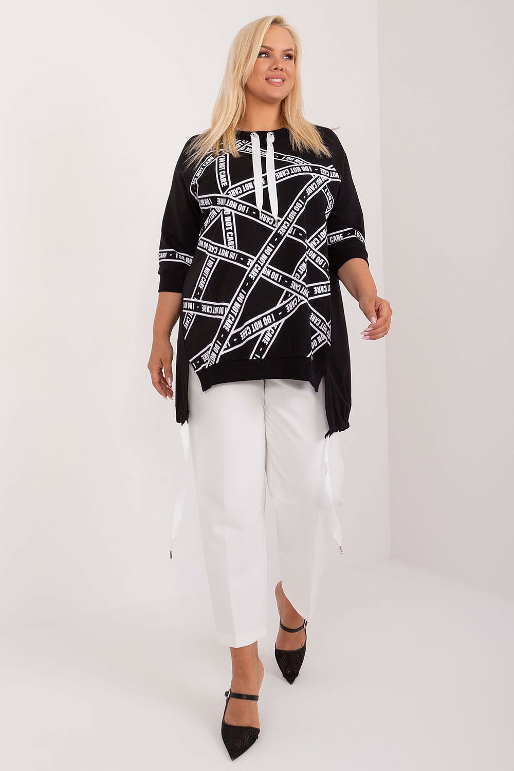 Woman wearing a black and white patterned top with white pants on a white background