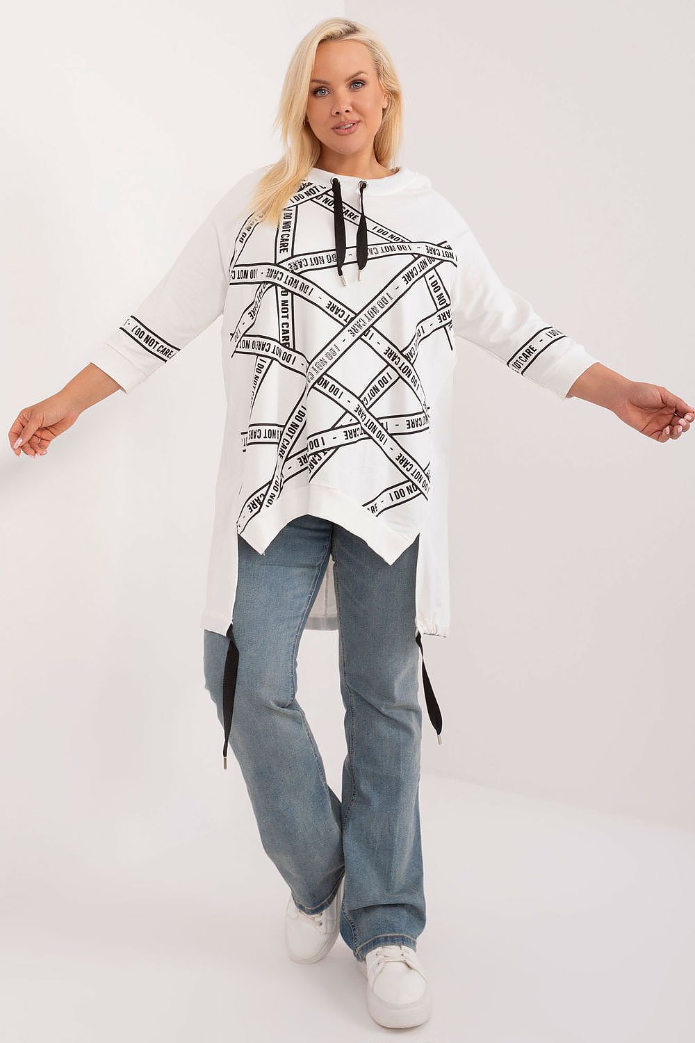 Woman wearing a white poncho with black patterns and text, standing against a white background