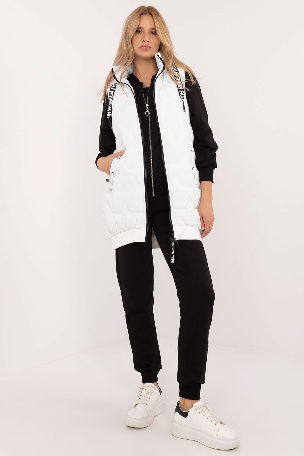 Woman wearing a black and white outfit with a long vest on a white background