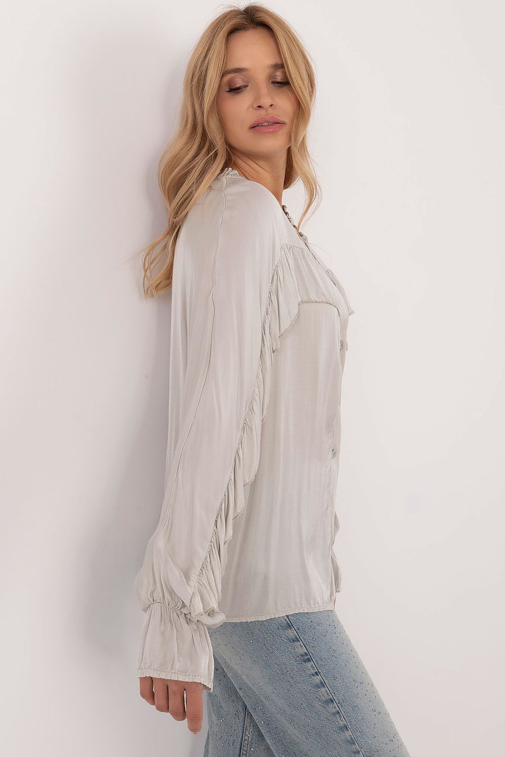 Woman wearing a light-colored blouse and jeans against a white background