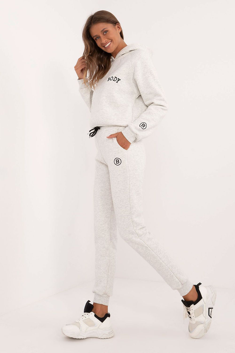 Woman wearing a white tracksuit with brand logos on a light background