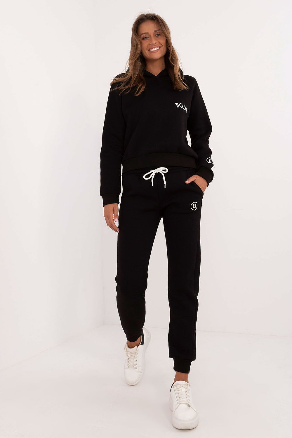 Person wearing a black tracksuit with brand logos on a white background