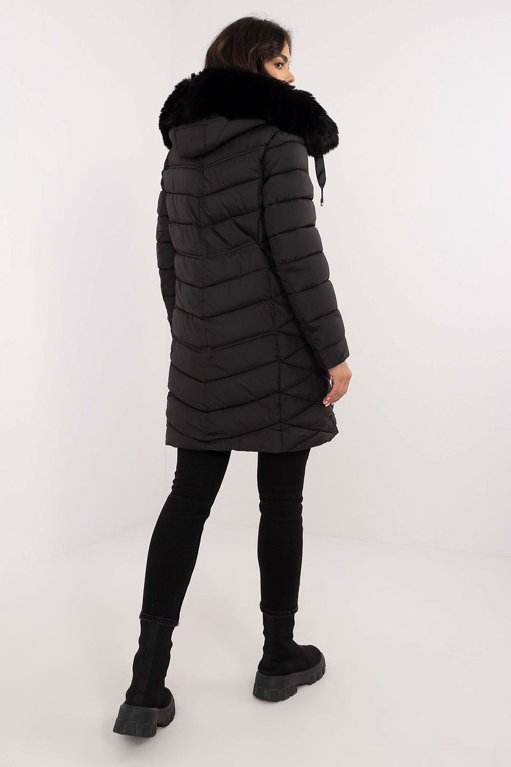 Person wearing a black puffer coat with fur hood on a white background