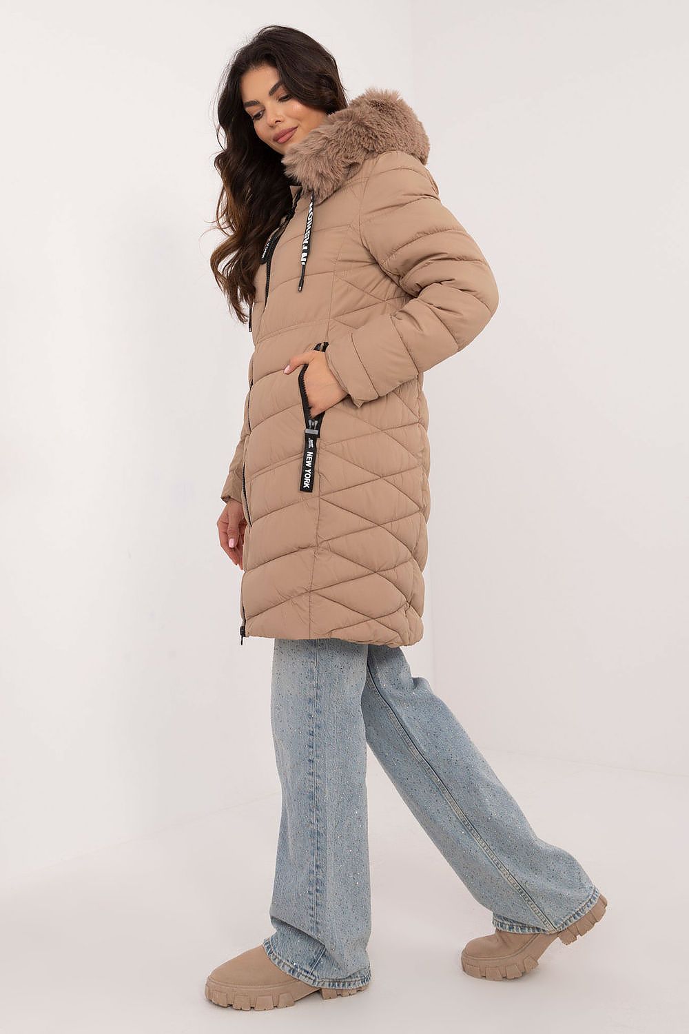 Woman wearing a beige quilted coat with fur hood on a white background