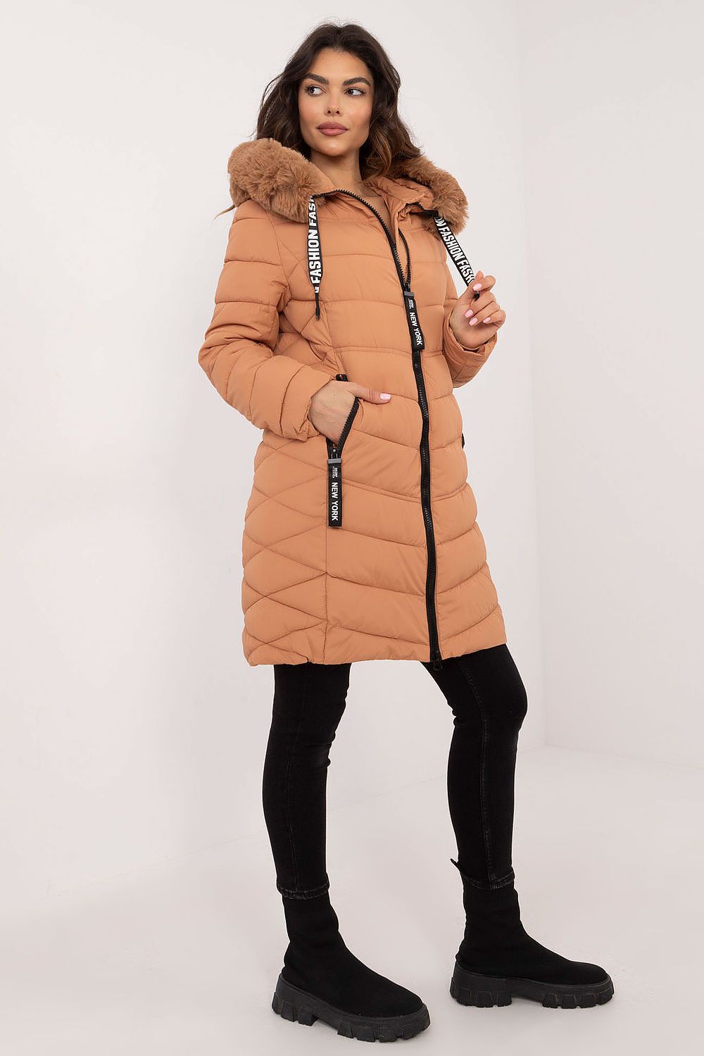 Woman wearing a long brown puffer coat with a fur-lined hood on a white background