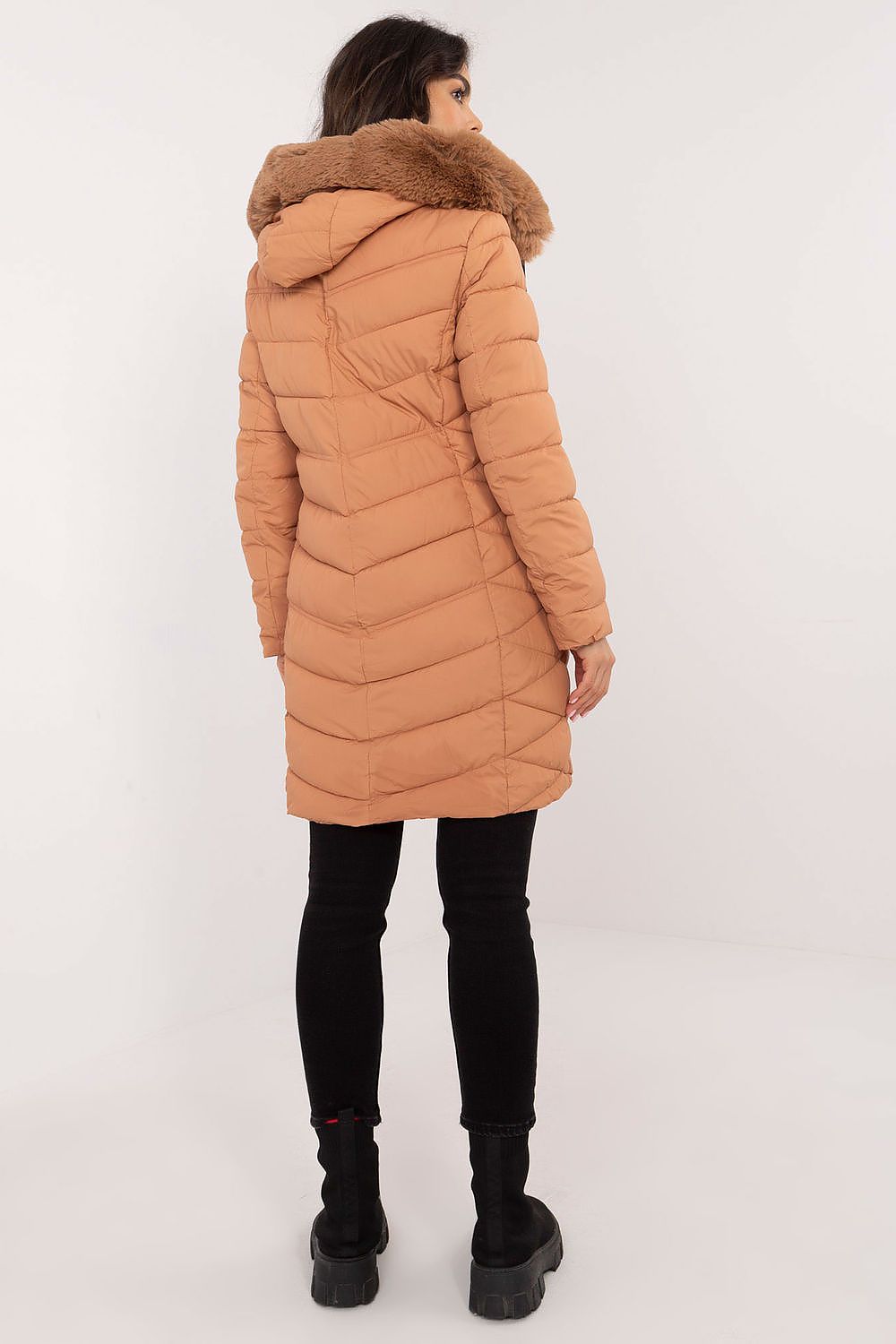 Person wearing a long brown puffer coat with a fur hood on a white background