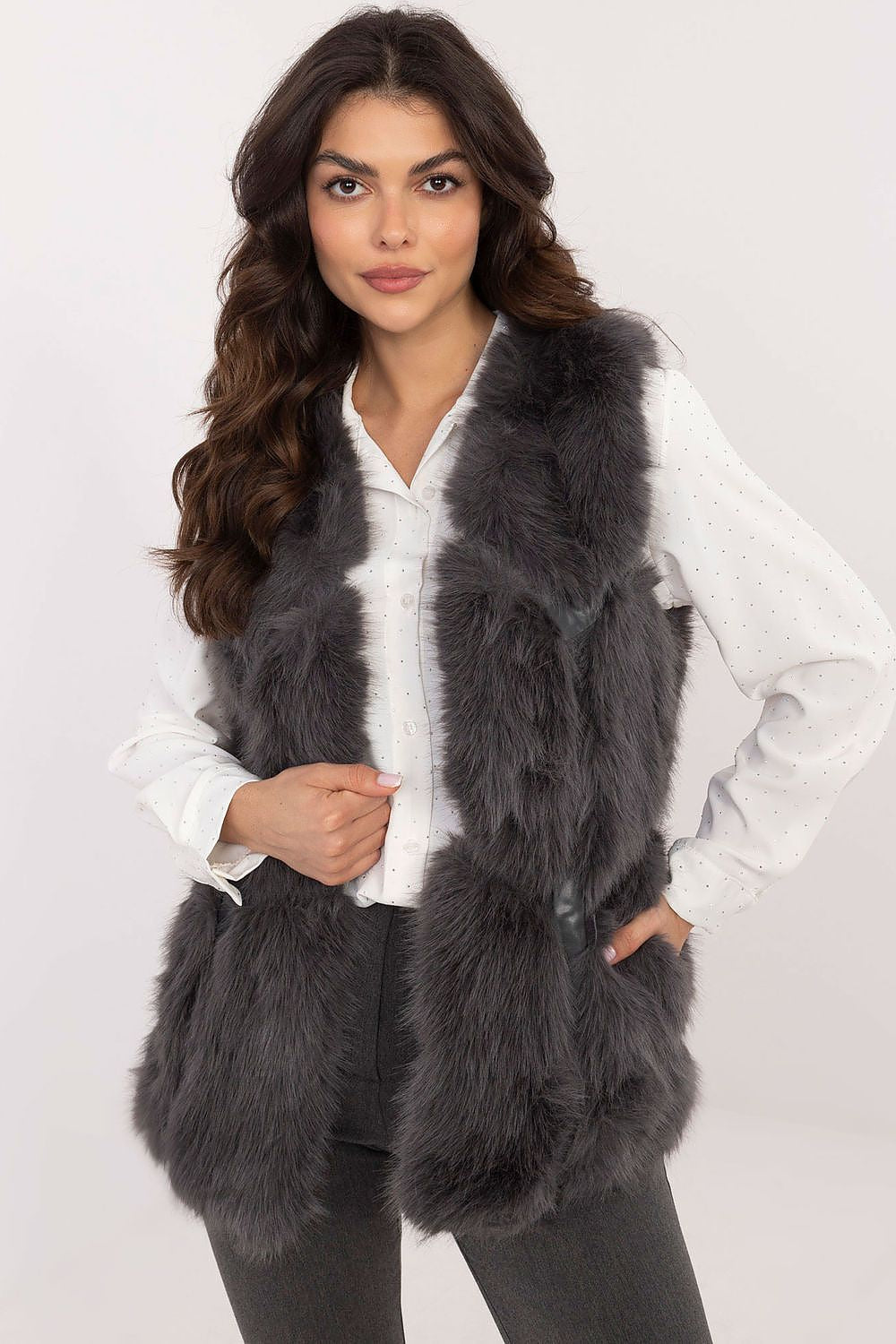 Woman wearing a dark gray fur vest over a white shirt on a white background
