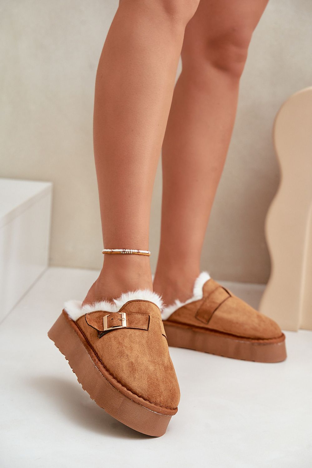 Brown slippers with white fur trim worn by a person on a light background