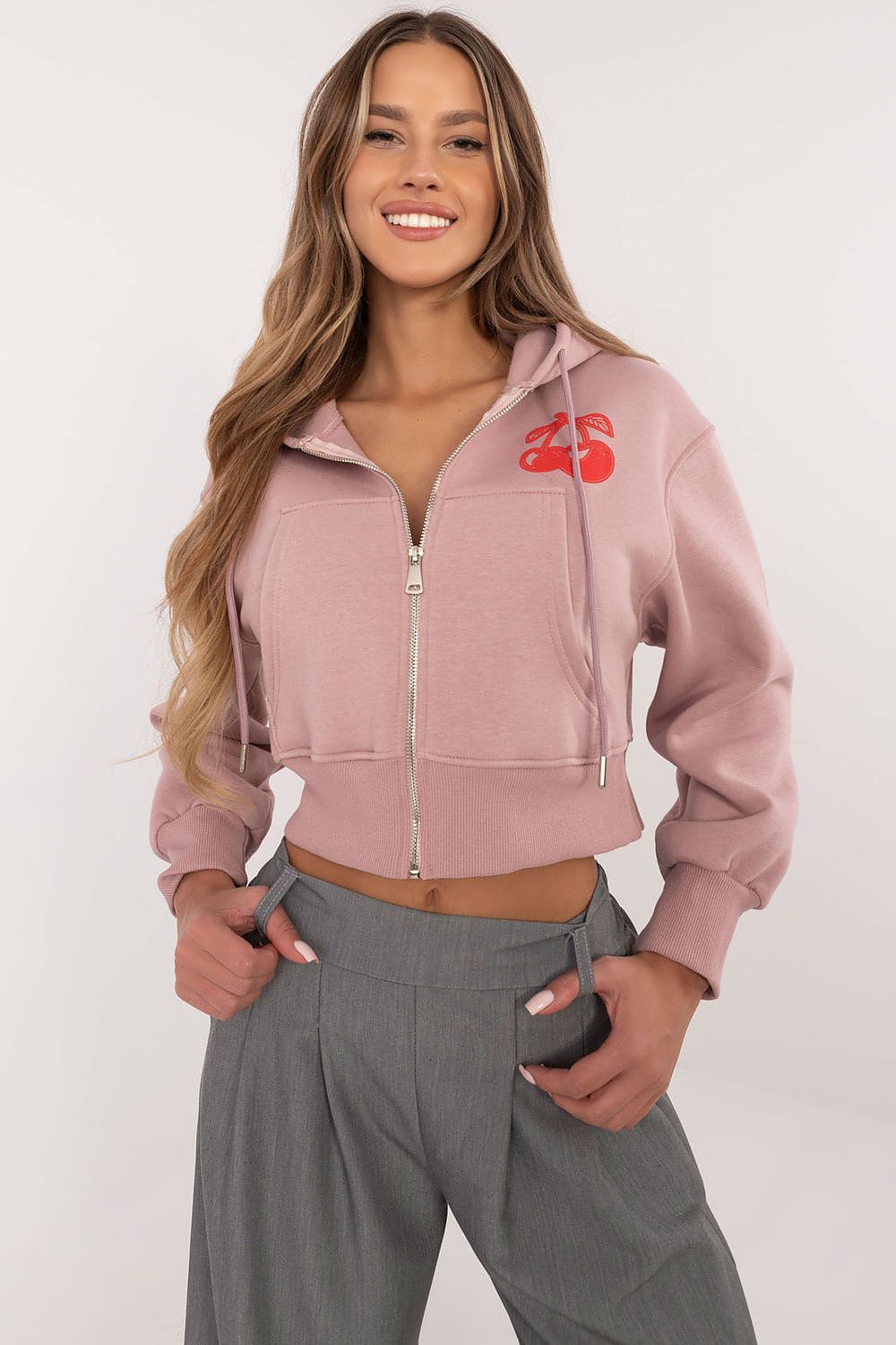 Woman wearing a pink hoodie with a logo and gray pants on a white background